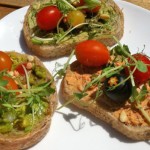 Three slices of bread with hummus, cherry tomatoes and greens on top