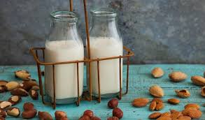 Two bottles of nut milk and several nuts around them on a blue table
