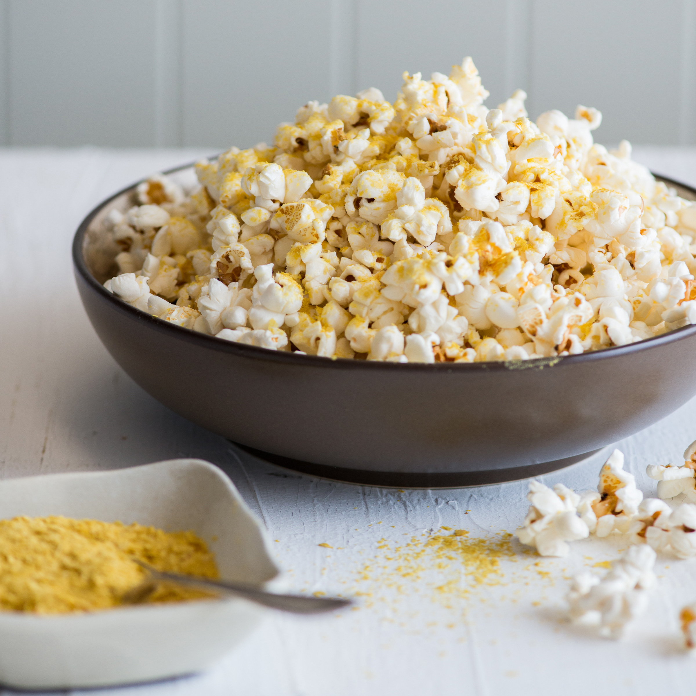 A big bowl of popcorn and a small bowl with nutritional yeast on a white table