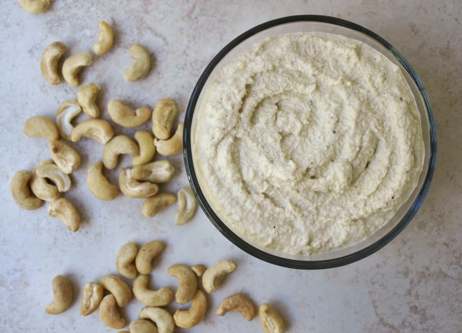 A bowl of cashew cheese, and some cashew nuts on a white surface