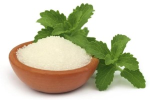 A few leaves of stevia next to a small bowl of stevia sweetener