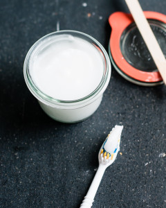 A small jar with diy toothpaste and a toothbrush next to it