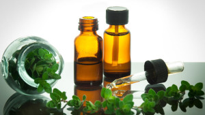 Two small bottles of oregano oil and a few oregano branches next to them